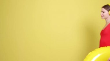 Kulaklıklı, şişirilebilir yüzüklü, renkli arka planda yürüyen genç bir kadın.