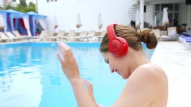 Güzel genç bayan tatil köyünde havuz kenarında müzik dinliyor.