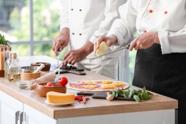 Aşçılar mutfakta lezzetli pizzalar pişiriyor.