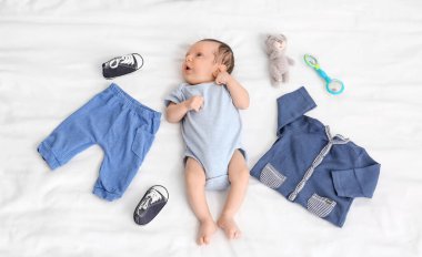 Giysileri ve oyuncaklarıyla yatakta uzanmış şirin bir bebek.