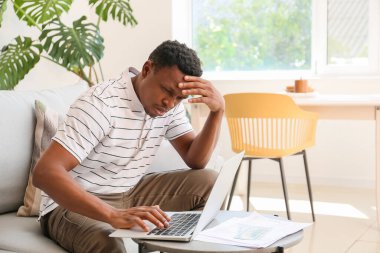 Evde dizüstü bilgisayarı olan stresli bir Afro-Amerikalı.