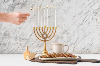 Hanuka için menoranın üzerinde mum yakan kadın masasında dreidels ve patatesli gözlemelerle