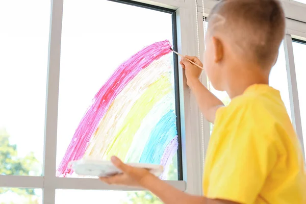 Little boy painting rainbow on window during Covid-19 quarantine at home