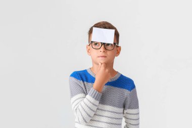 Thoughtful boy with blank note paper on his forehead against light background clipart