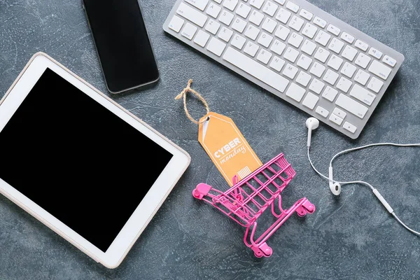 Computer keyboard with tablet PC, mobile phone, shopping cart and tag with text CYBER MONDAY on dark background