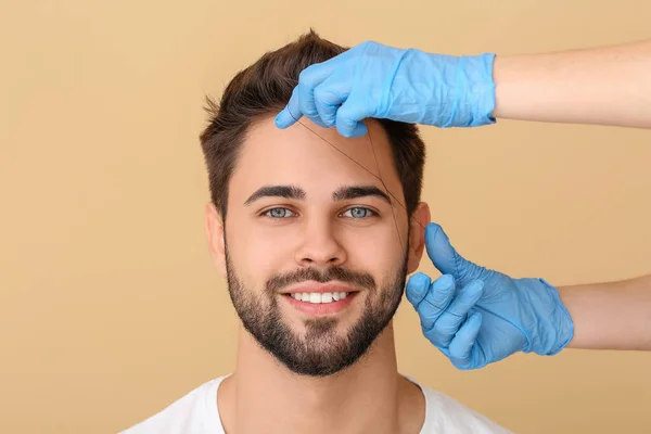 Young man undergoing eyebrow correction procedure on color background