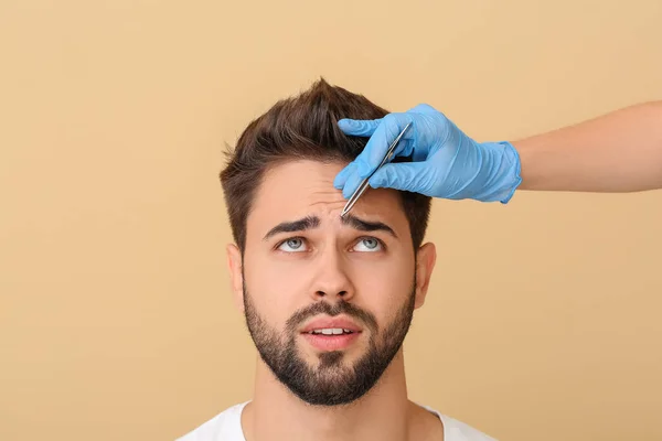 Young man undergoing eyebrow correction procedure on color background