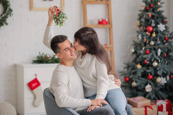 Молодая Женщина Целует Своего Мужа Омелой Бранч Дома Канун Рождества — стоковое фото
