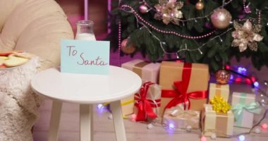 Evde Noel Baba 'ya mektup yazan bir kadın masaya kurabiye ve süt koyuyor.