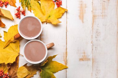 Beyaz ahşap arka planda sonbahar yapraklı sıcak kakao içeceği.