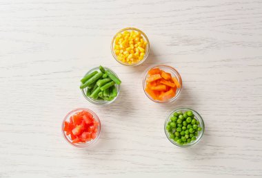 Beyaz ahşap arka planda farklı donmuş sebzelerle dolu kaseler.