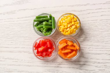 Beyaz ahşap arka planda farklı donmuş sebzelerle dolu kaseler.