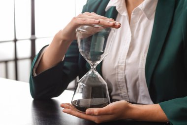 Ofisinde kum saati olan genç bir iş kadını, yakın plan.