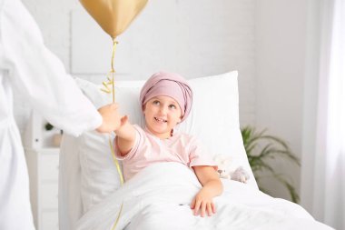 Altın balonlu bir doktor ve klinikte kemoterapi gören küçük bir kız. Çocukluk kanseri farkındalığı