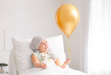 Klinikte kemoterapi gören altın balonlu küçük bir kız. Çocukluk kanseri farkındalığı