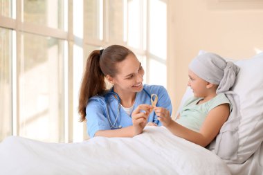 Klinikte altın kurdeleli hemşire ve küçük kız. Çocukluk kanseri farkındalığı