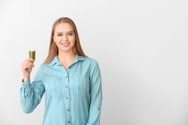 Açık arkaplanda buğday çimi suyu olan genç bir kadın.