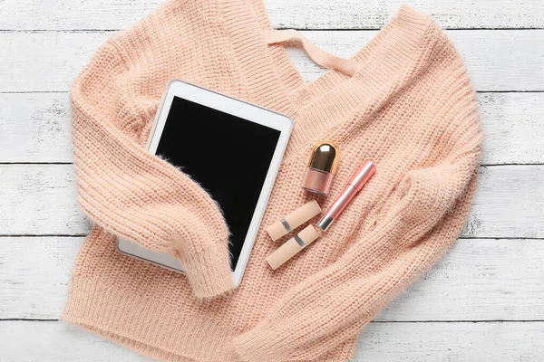 Female sweater with tablet computer and makeup cosmetics on table
