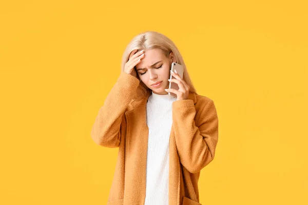 Stressed young woman talking by mobile phone on color background