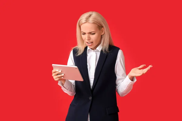 Stressed young businesswoman with tablet computer on color background