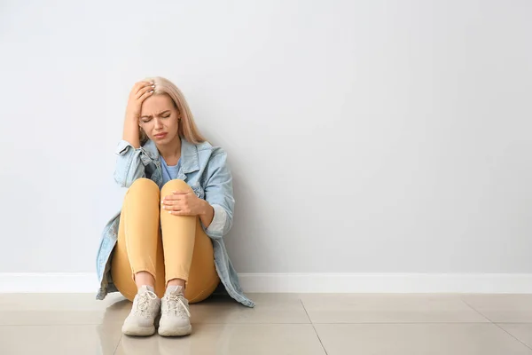 Stressed young woman sitting near light wall