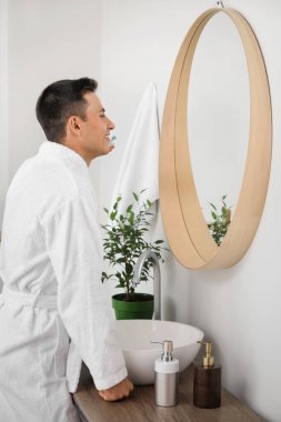 Genç adam banyoda dişlerini fırçalıyor.