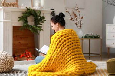 Evinde sıcak ekose kitap okuyan güzel genç bir kadın.