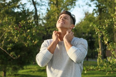 Alerjisi olan genç bir adam dışarıda kaşınıyor.