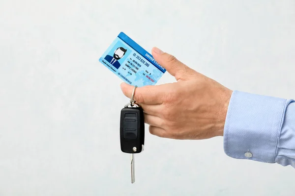 Male hand with driving license and car key on light background