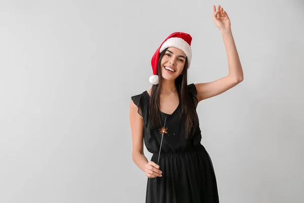 サンタの帽子の美しい若い女性と光の背景にクリスマスの輝き — ストック写真