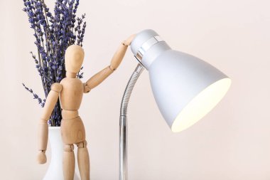 Lambalı ahşap manken ve arka planda çiçekler.