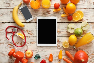 Fresh products, tablet computer, mobile phone and stethoscope on white wooden background. Diet concept