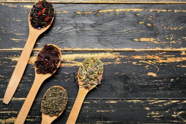 Koyu ahşap arka planda farklı meyve çayları olan kaşıklar.