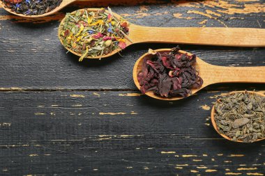 Koyu ahşap arka planda farklı meyve çayları olan kaşıklar.