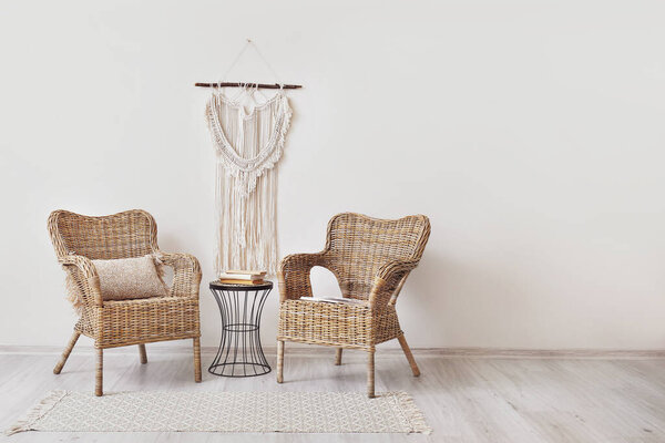 Stylish armchairs with pillow and table with books near light wall in room