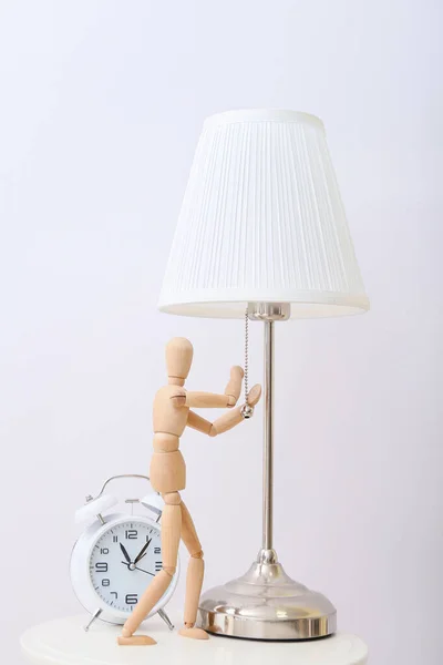 ライトを背景にテーブルの上にランプと目覚まし時計を持つ木製のマネキン — ストック写真