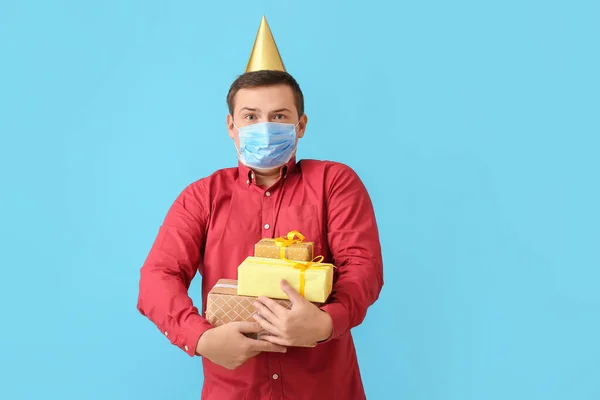 Young man in medical mask and with Birthday gifts on color background