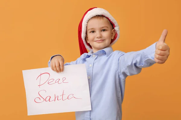 给圣诞老人写信的小男孩在彩色背景上表现出大拇指向上的姿势 — 图库照片