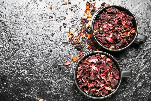Cups with dry hibiscus tea on dark background