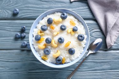 Bir kase lezzetli pirinç pudingi yaban mersini ve ahşap masada kaju.