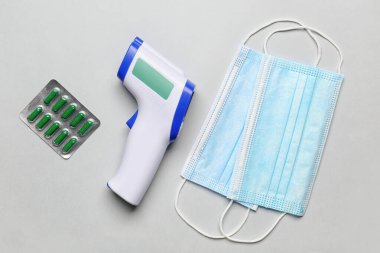 Infrared thermometer, masks and pills on light background