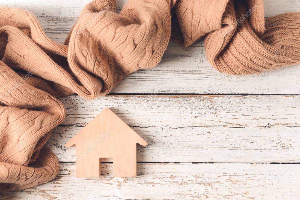 Figure of house and warm scarf on wooden background. Concept of heating season