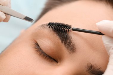 Young man undergoing eyebrow correction procedure in beauty salon, closeup clipart