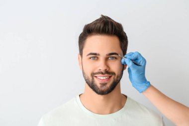 Genç adam arka planda kaş düzeltme prosedüründen geçiyor.