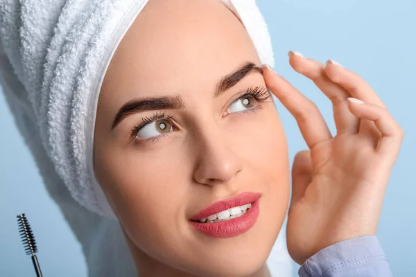 Young woman undergoing eyebrow correction procedure on color background