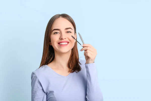 Young woman with tools for eyebrow correction procedure on color background