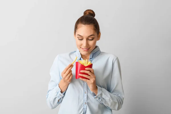 Young woman with french fries on light background