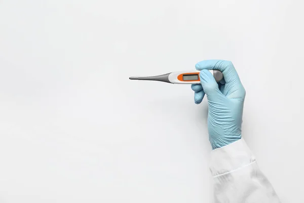 Hand of doctor with thermometer on light background