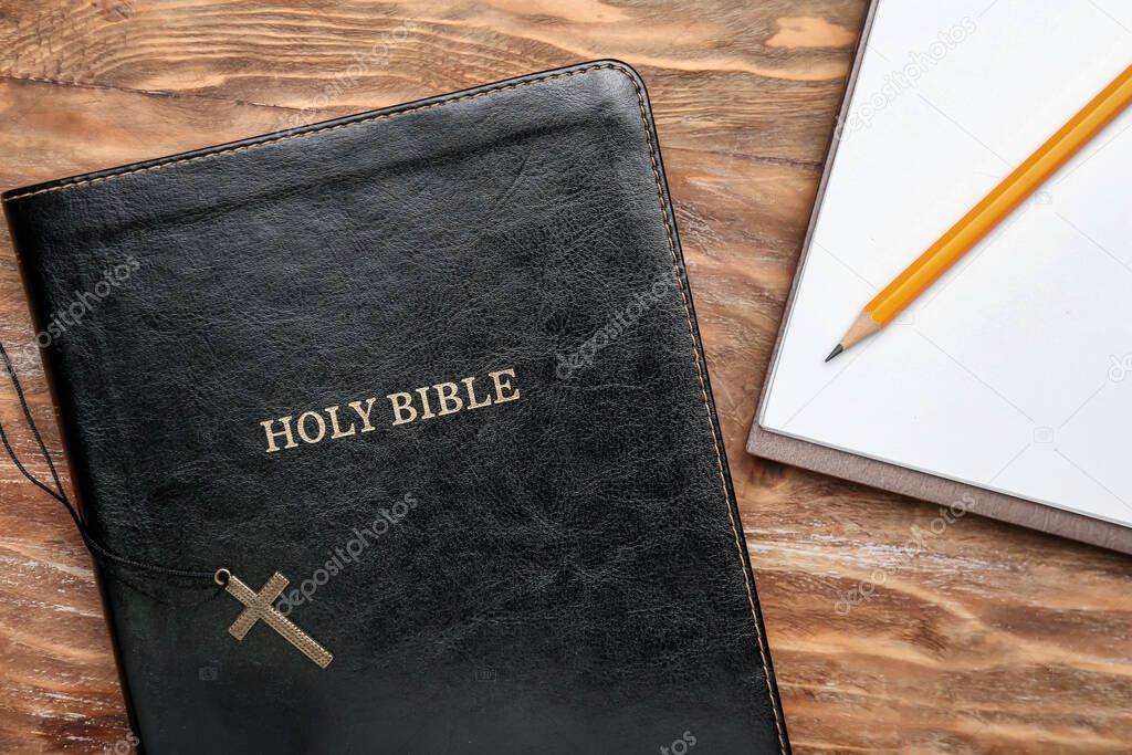 Holy Bible, cross and notebook on wooden table