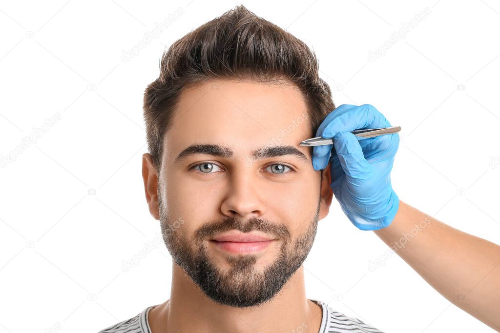 Young man undergoing eyebrow correction procedure on white background
